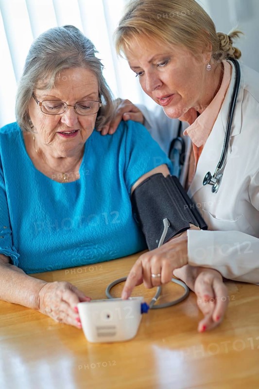 Senior adult woman learning from female doctor to use blood pressure machine