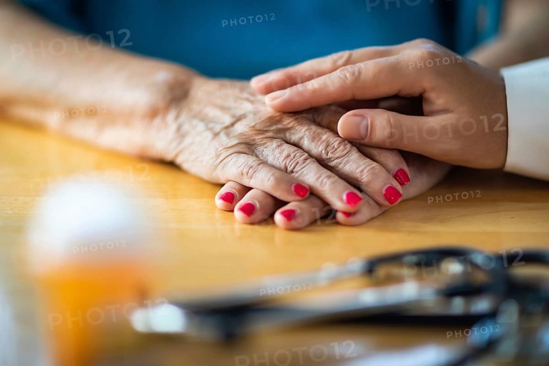 Younger female hands touching senior adult woman hands near stethoscope and medicine bottle
