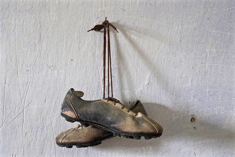 Hanging old leather football boots on nail in front of white wall