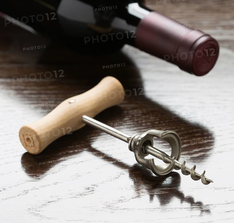 Abstract wine bottle and corkscrew laying on a reflective wood surface