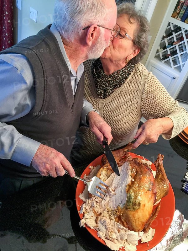 Senior adult couple cutting the holiday Turkey together in the kitchen
