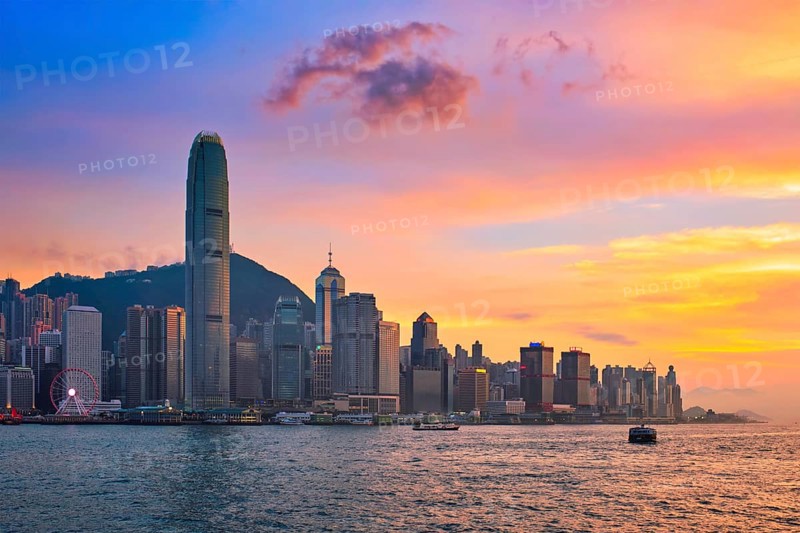 Hong Kong skyline cityscape downtown skyscrapers over Victoria Harbour in the evening with junk tourist ferry boat on sunset with dramatic sky. Hong Kong