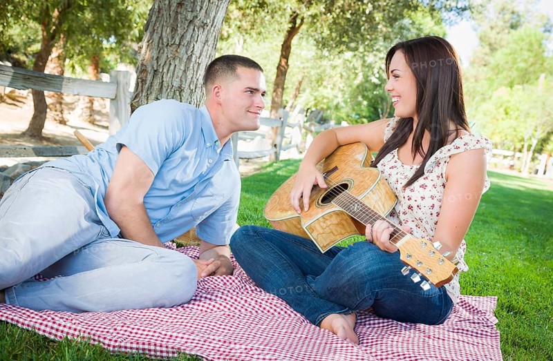 Young adult girl playing guitar with boyfriend in the park