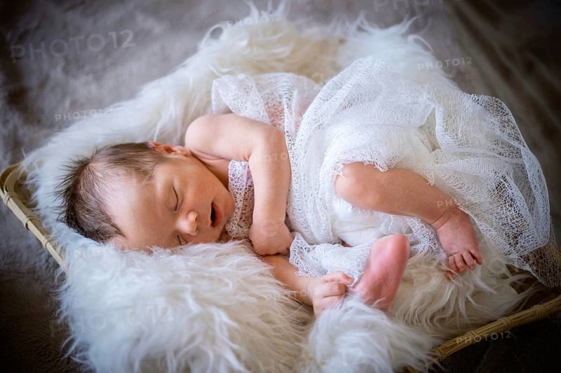 Cute newborn baby boy sleeping in the basket on fluffy blanket