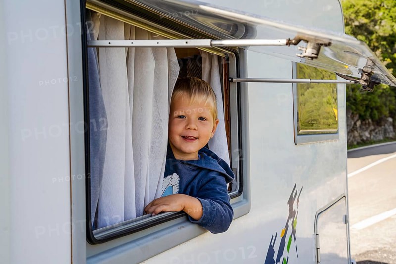Happy small boy looking through the RV's window parked along the road