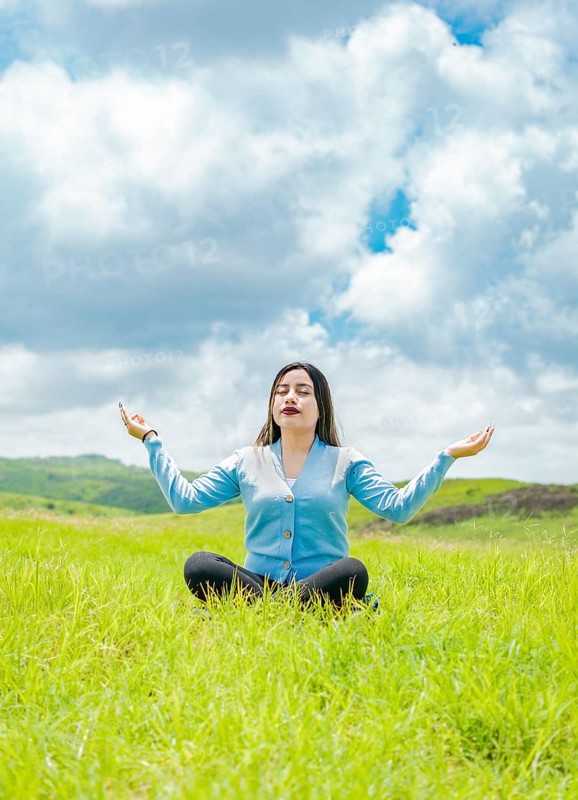 Young woman doing yoga on the grass in the field with blue sky in the background