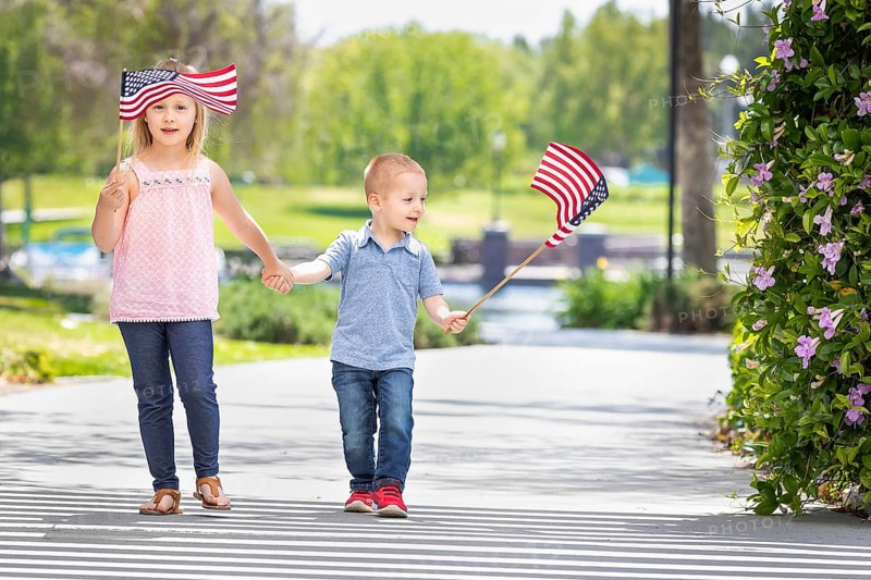Young sister and brother waving american flags at the park