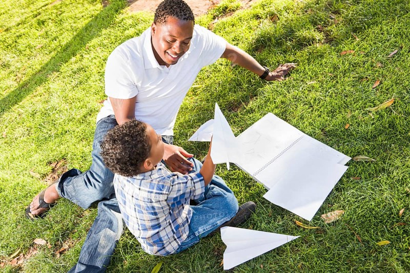 Happy african american father and mixed-race son playing with paper airplanes in the park