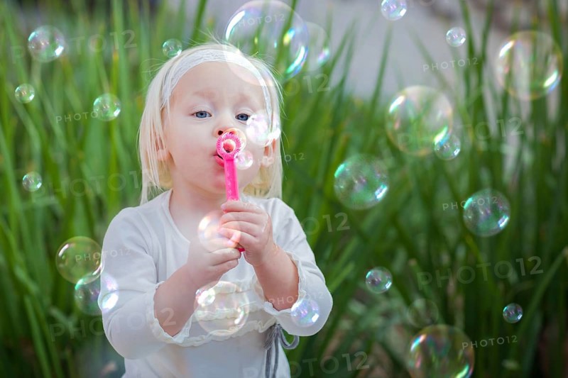 Adorable little girl sitting on bench having fun with blowing bubbles outside