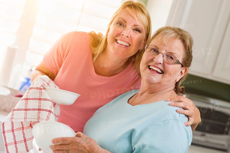 Portrait of smiling senior adult woman and young daughter at sink in kitchen