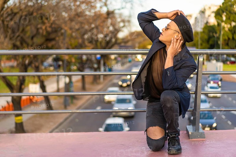 Latino gay male with makeup wearing trendy hat posing on a bridge