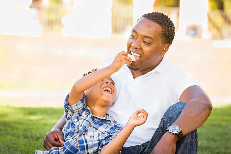 African american father and mixed-race son eating an apple in the park