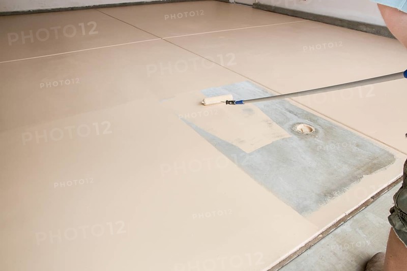 Worker painting floor of garage with roller