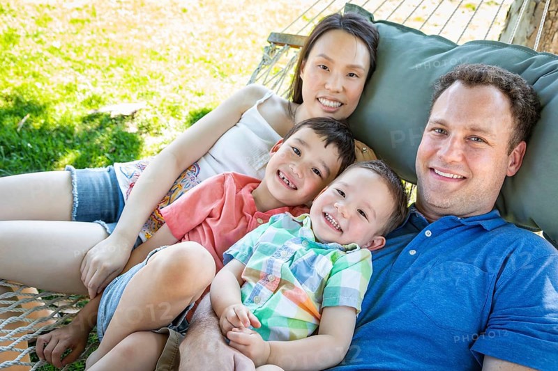 Caucasian father and chinese mother relaxing in hammock with mixed-race sons