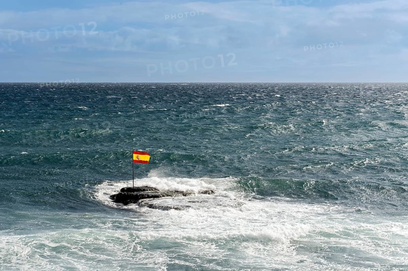 A Spanish flag on rocks in the Atlantic Ocean during windy weather in Pozo Izquierdo Bay