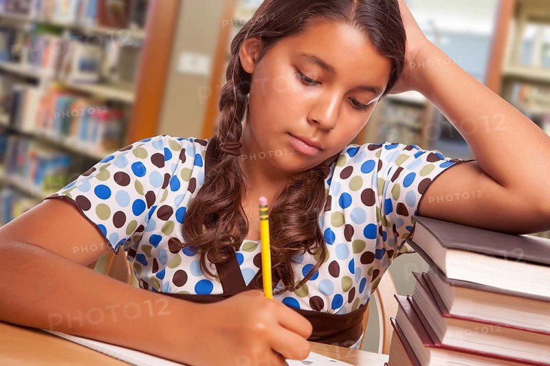 Hispanic girl student with pencil and books studying in library