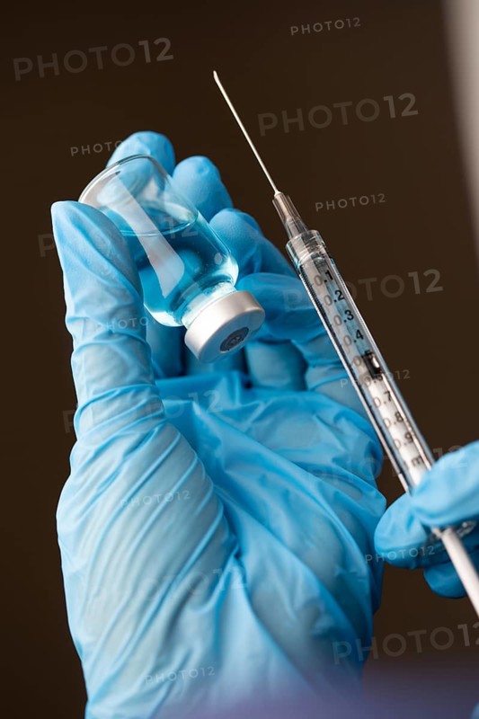 Doctor or nurse wearing surgical gloves holding vaccine vial and medical syringe