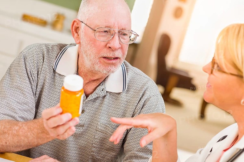 Doctor or nurse explaining prescription medicine to attentive senior man