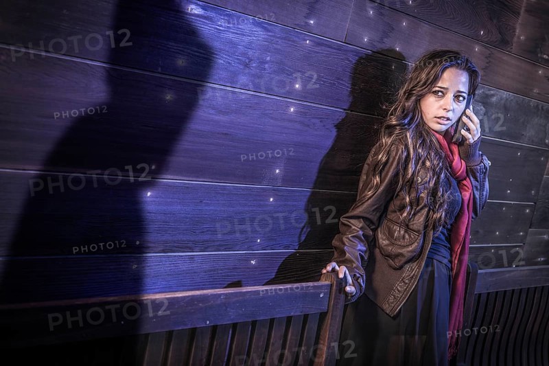 Scared young adult woman uses cell phone as mysterious male shadow figure lurks nearby