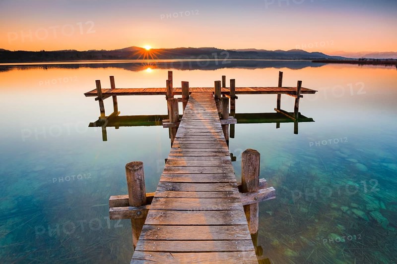 Holzsteg am Pfaeffikersee im Gegenlicht bei Sonnenaufgang mit Blick zum Bachtel und Glaernisch im Hintergrund