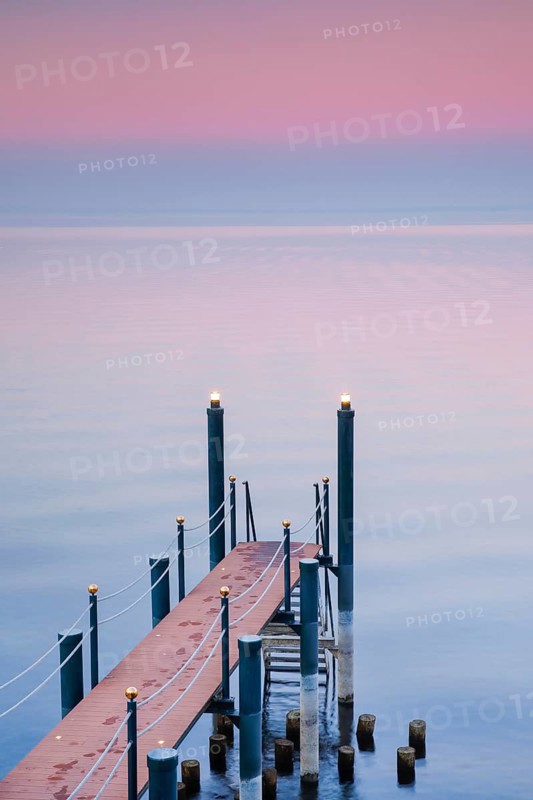 Rosa Abendstimmung ueber dem Bodensee mit beleuchtetem Badesteg zum See