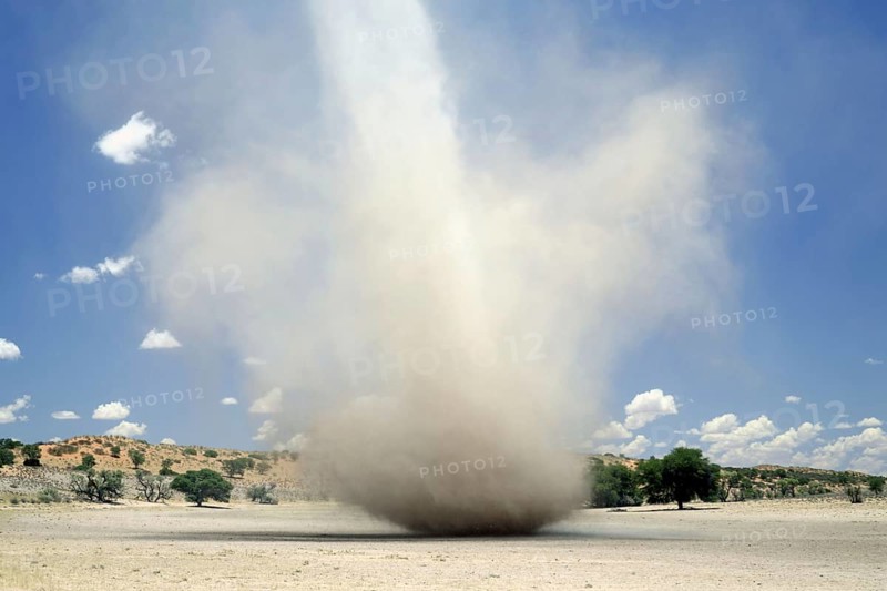 Dust devil cyclone crosses dry river bed in semi-desert