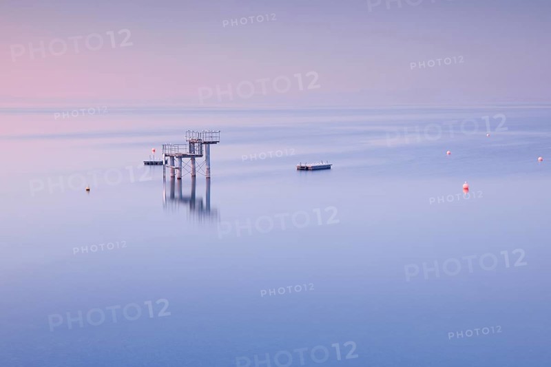 Rosa-violette Abendstimmung ueber dem Bodensee mit Blick zum Sprungturm und den Flossen der Freibadanlage Horn inmitten des Sees