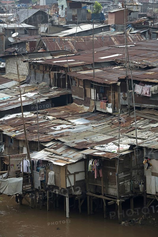 Stilted shacks with corrugated iron roofs beside river in city