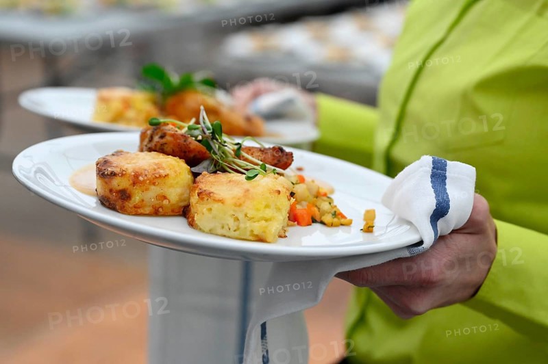 Service staff with plate of corn poulard breast with potato gratin and root vegetables