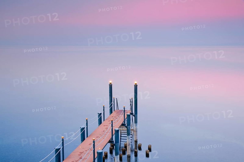 Rosa Abendstimmung ueber dem Bodensee mit beleuchtetem Badesteg zum See