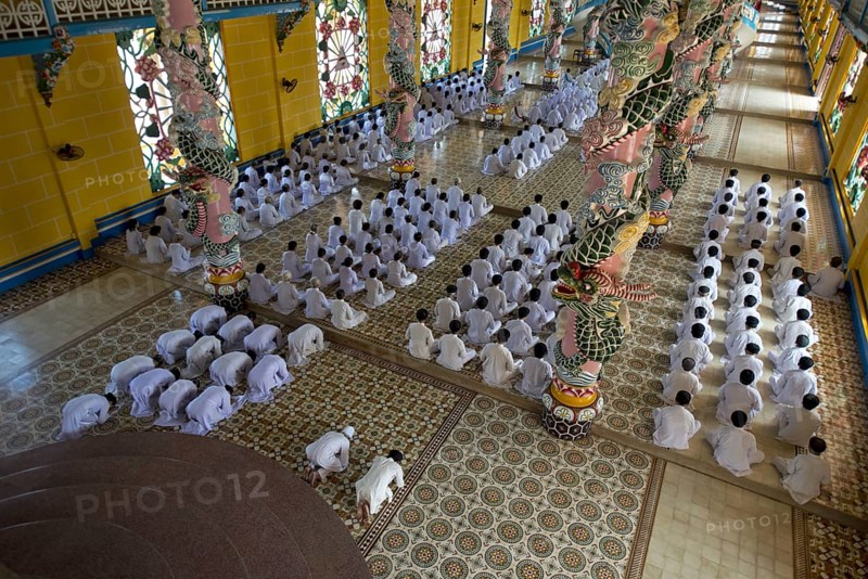 Caodaist disciples sitting beside colourful columns with dragons during ceremony