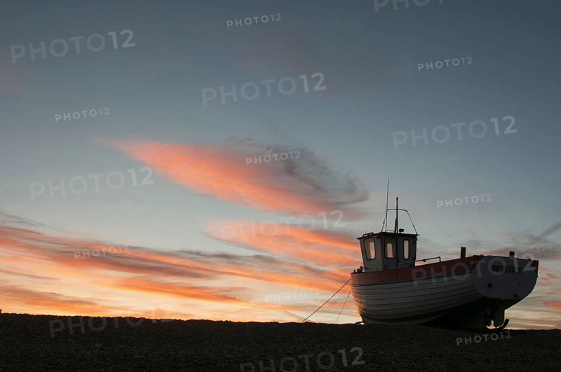 Fishing boat hauled up on shingle beach at sunset