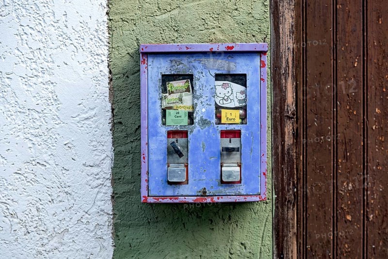 Old chewing gum machine filled with chewing gum and children's toys on the wall of a house