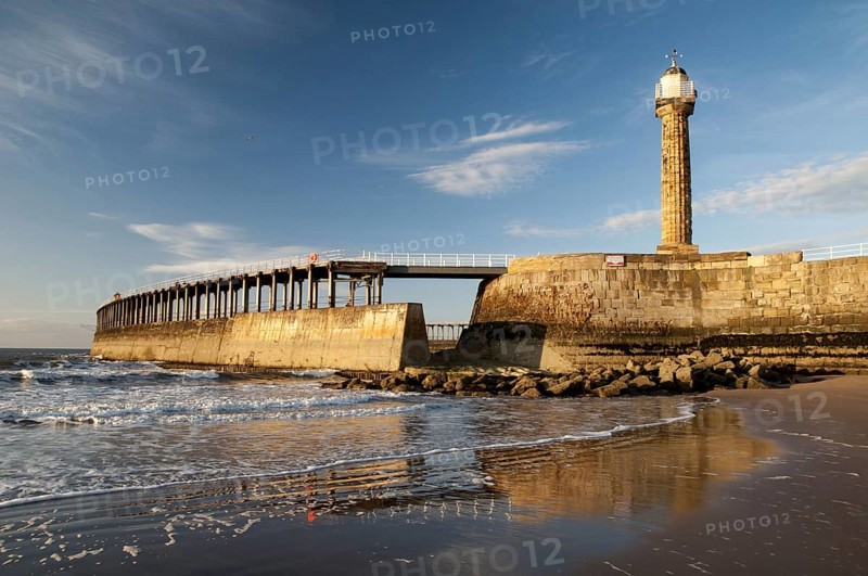 View of beach and pier with 19th century stone lighthouse in the evening sun