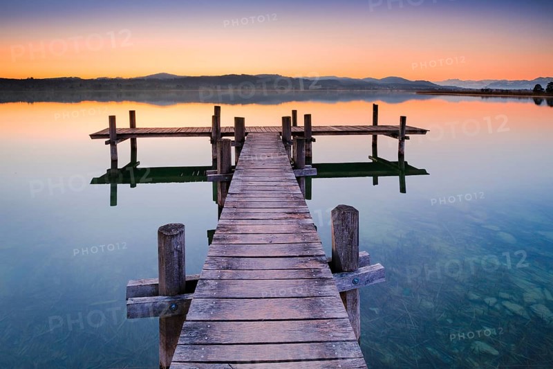 Holzsteg am Pfaeffikersee im Gegenlicht bei Sonnenaufgang mit Blick zum Bachtel und Glaernisch im Hintergrund