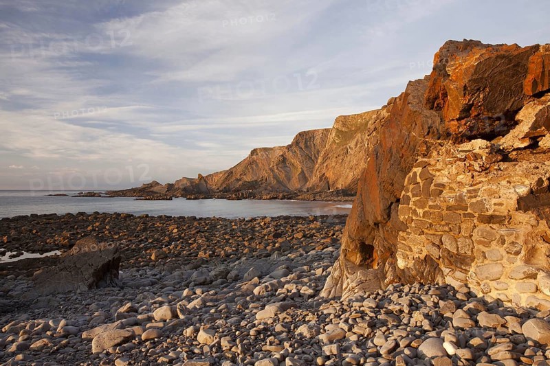Man-made dyke and coastal cliff with folded layers at sunset