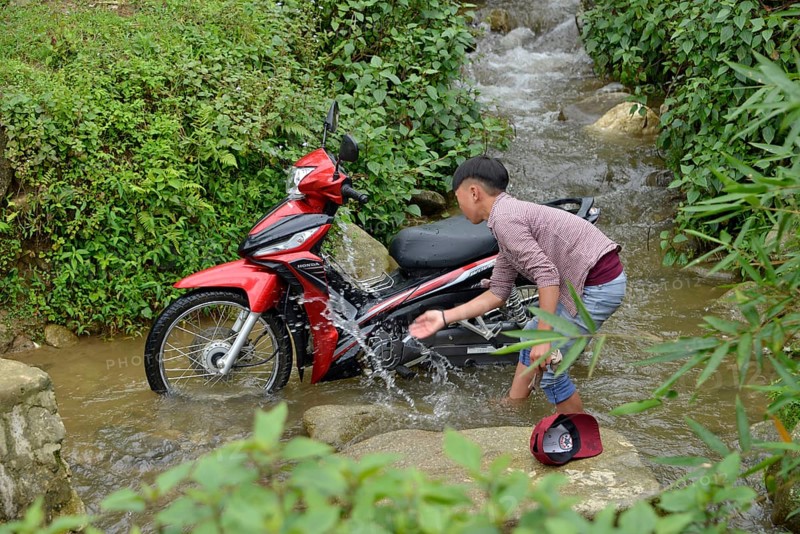 Boy washes motorbike in stream