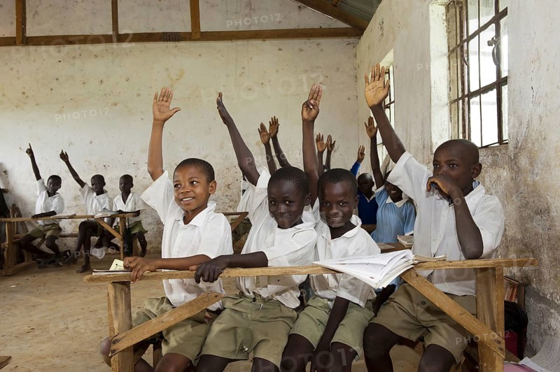 Children with their hands up in the classroom of a rural school