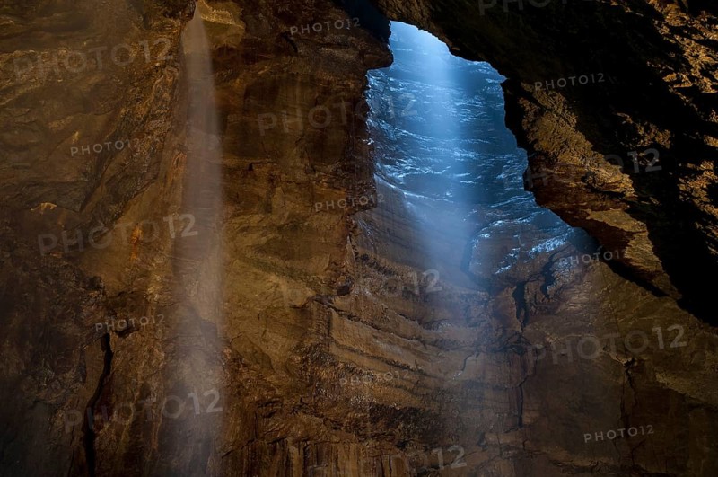View of upland stream waterfall flowing down chasm into chamber of cave