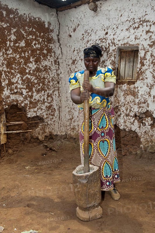 Woman grinding cassava with a post and wooden pot to create Cassava flour to be used in baking. Rwanda