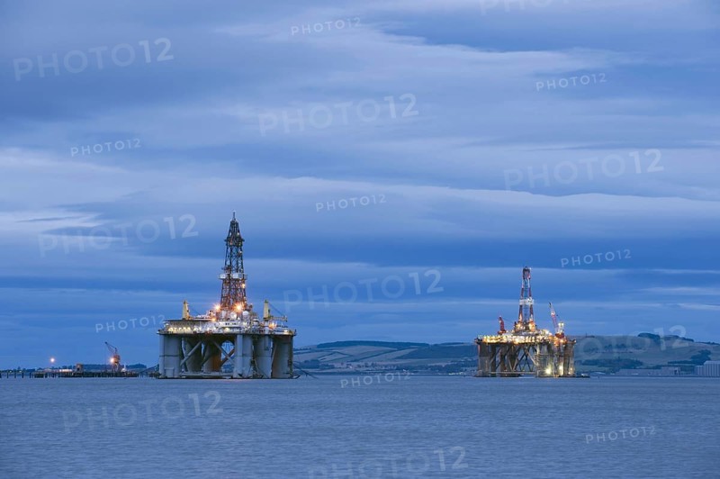 Oil rigs moored in sea near coast at dusk