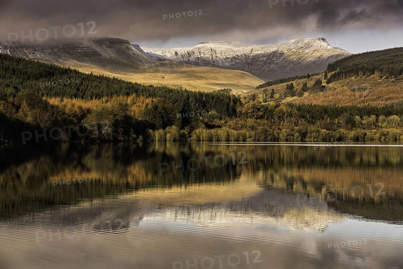 Trees and snow-capped hills reflected in the reservoir at sunrise