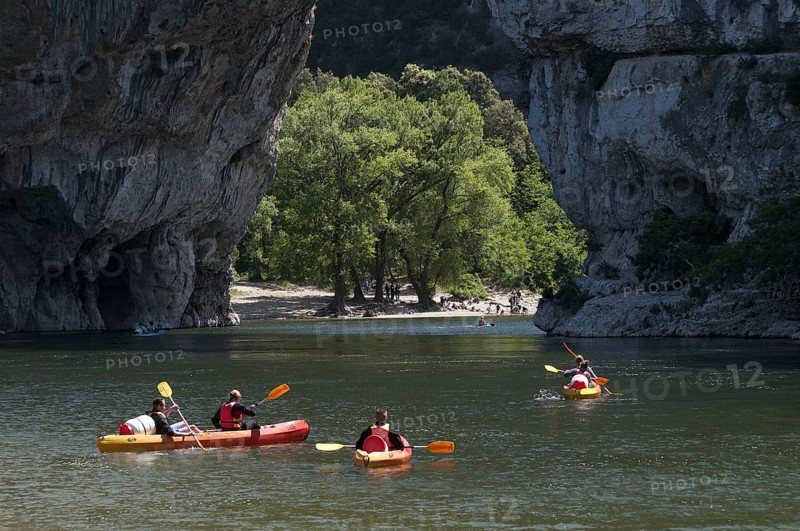 People canoeing on river towards limestone arch