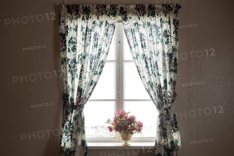 Fenster von innen mit gebluemten Gardinen und Blumenstrauss in einem alten verlassenen Haus. Vaermland