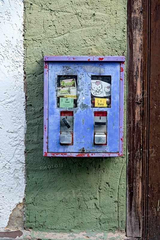 Old chewing gum machine filled with chewing gum and children's toys on the wall of a house