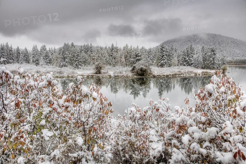 View of mountain range and forested river valley with trees in autumn colours and snow