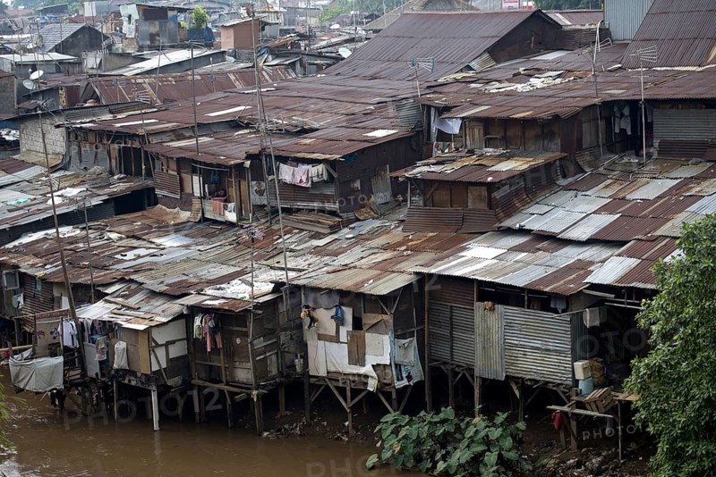 Stilted shacks with corrugated iron roofs beside river in city