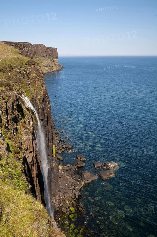 View of the coastline with a waterfall cascading over cliffs into the sea with Kilt Rock in the background