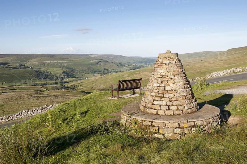 Cairn and bench at highland viewpoint overlooking valley marking Muker parish boundary