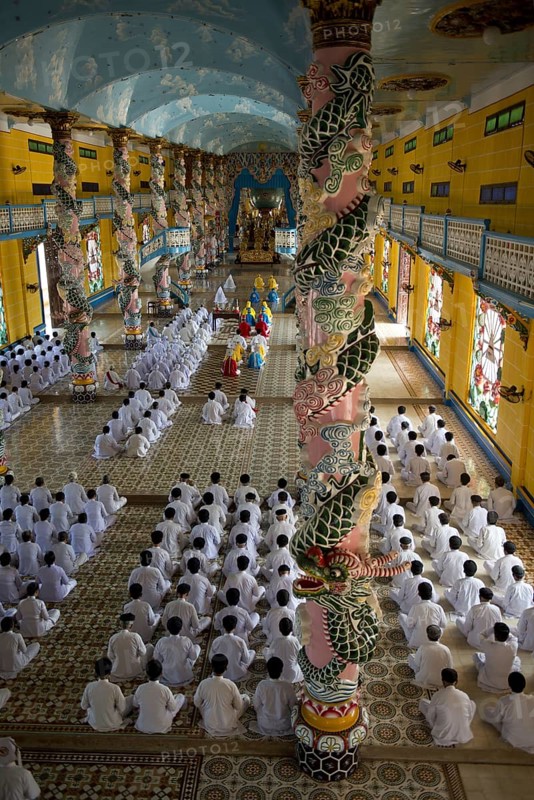 Caodaist disciples sitting beside colourful columns with dragons during ceremony